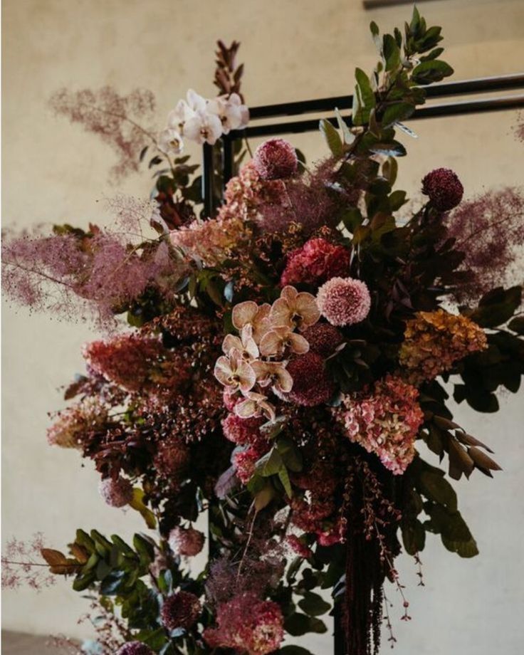 an arrangement of flowers and greenery in a vase on a table next to a mirror