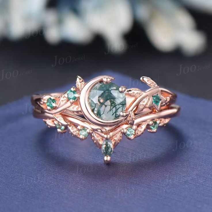 a close up view of a ring with green stones and leaves on the side,