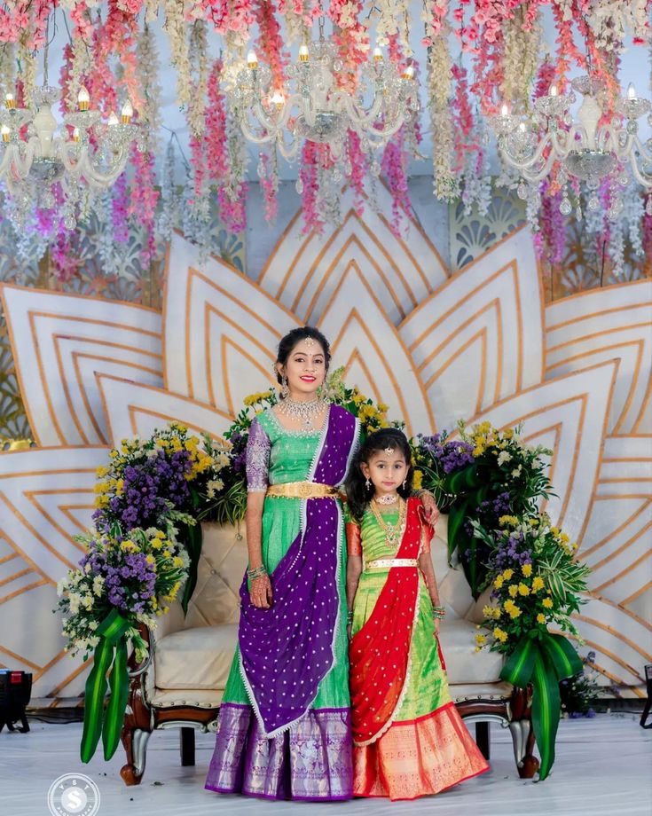 two women standing next to each other in front of a chandelier filled with flowers