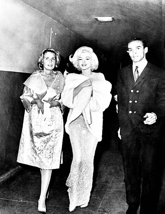 two women and a man are walking down the hallway in an old black and white photo