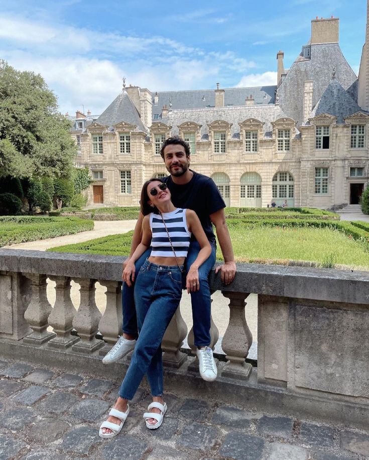 a man and woman sitting on a stone wall in front of a castle