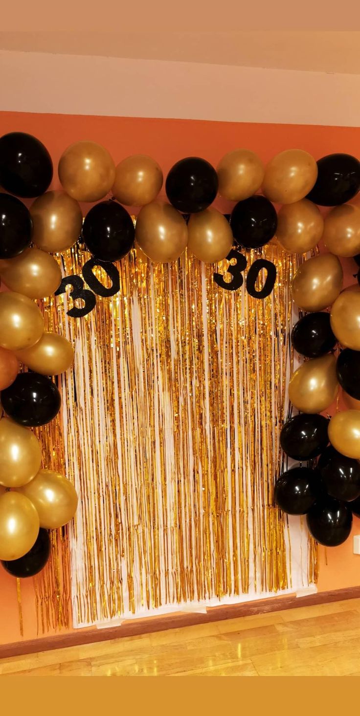 balloons and streamers decorate the entrance to a 30th birthday party with black, gold and white decorations