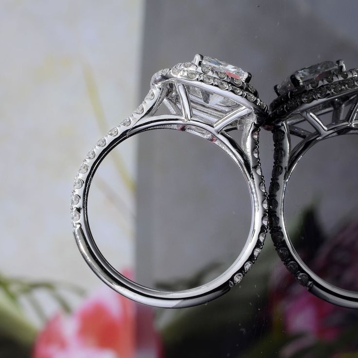 two wedding rings sitting next to each other on top of a glass table with flowers in the background