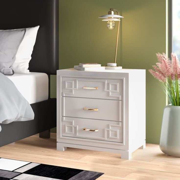 a white nightstand sitting on top of a wooden floor next to a bed