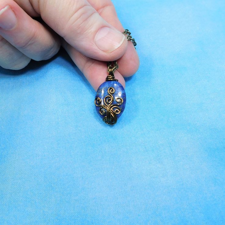 A 3/4 inch by 1/2 inch oval Lapis Lazuli bead is artistically hand wire wrapped with non tarnish vintage bronze colored copper wire. The warm tones of copper bring out the flashes of pyrite from within the stone. The pendant is beautifully simple, but distinctively unique. A piece that will be a treasured part of any woman's jewelry collection. This artistic pendant comes with a FREE coordinating chain with lobster claw clasp, measured to your preferred length. Your one of a kind necklace is rea Wire Pendant Necklace As A Gift, Wire Pendant Necklace For Gift, Artisan Oval Cabochon Jewelry Gift, Unique Hand Wrapped Oval Pendant Jewelry, Adjustable Blue Oval Jewelry, Adjustable Oval Necklace As Gift, Adjustable Oval Necklace Perfect For Gifts, Artistic Blue Metal Jewelry, Handmade Blue Oval Bead Jewelry