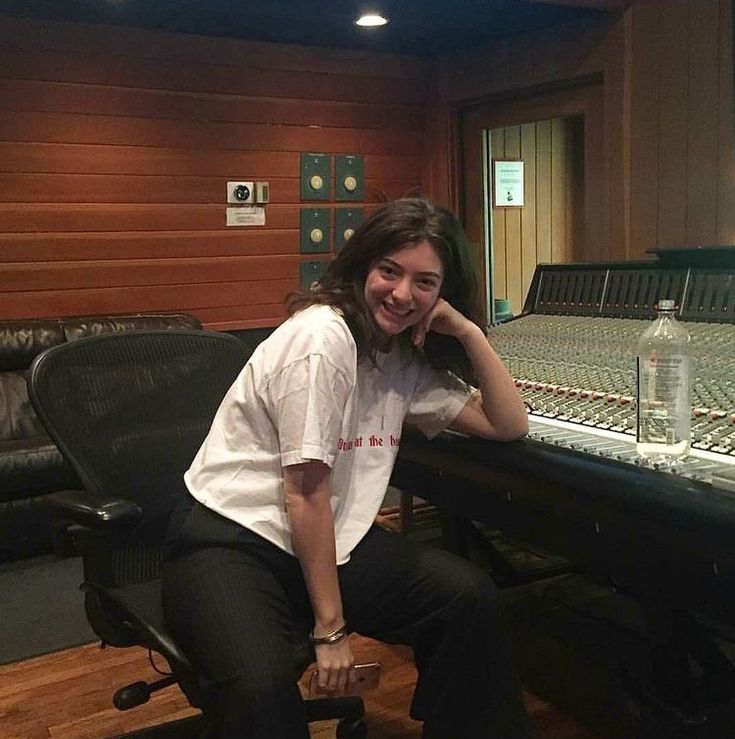 a woman sitting in front of a mixing desk with sound equipment behind her smiling at the camera