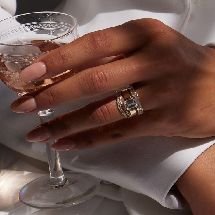 a person holding a wine glass with two wedding rings on it's fingers and wearing a white dress shirt