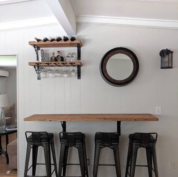 three stools and a table in the middle of a room with two mirrors on the wall