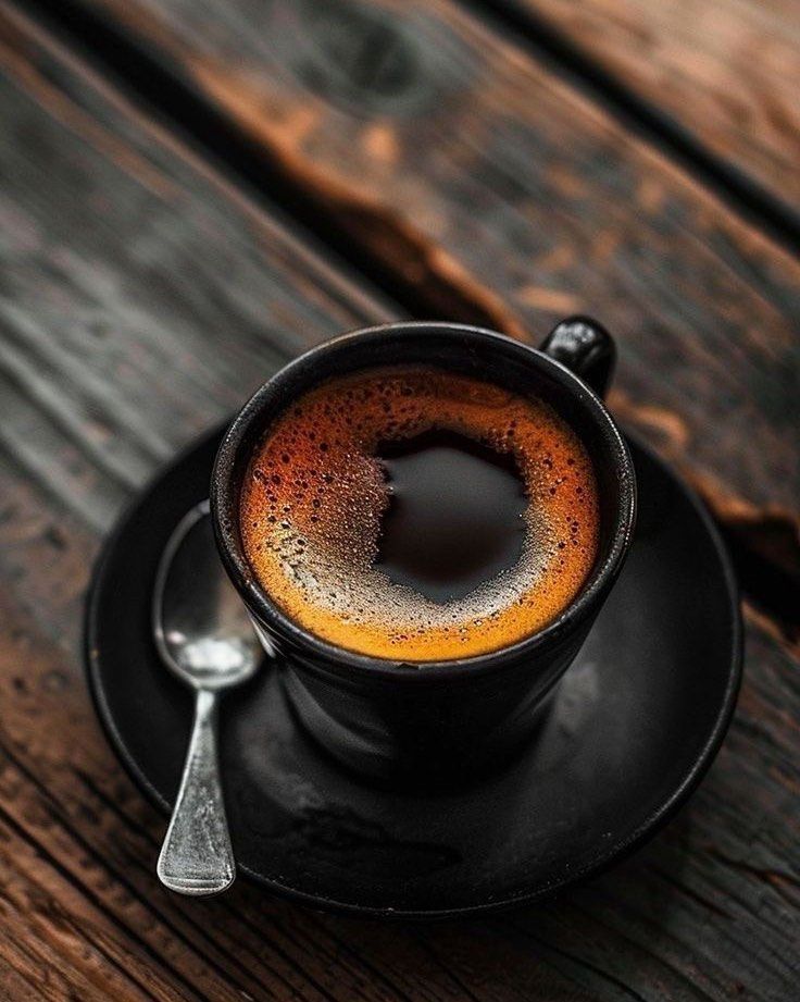 a cup of coffee sitting on top of a black saucer with a spoon next to it