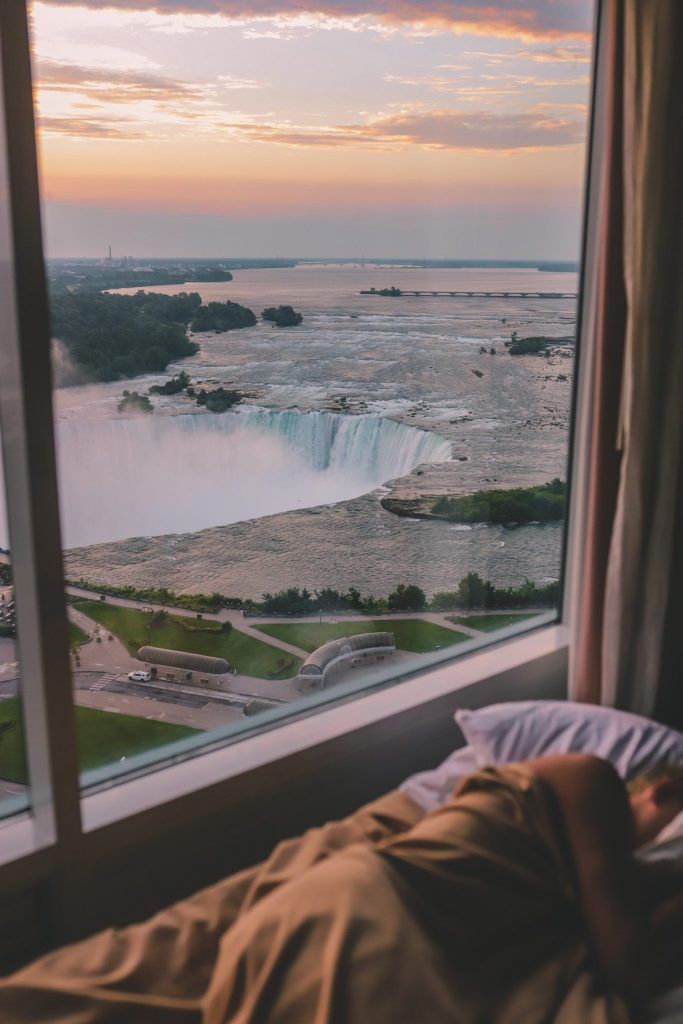 a person is laying in bed looking out the window at niagara falls from their hotel room