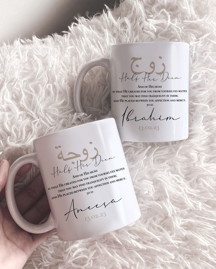 two white coffee mugs with arabic calligraphy on them, one being held up by someone's hand