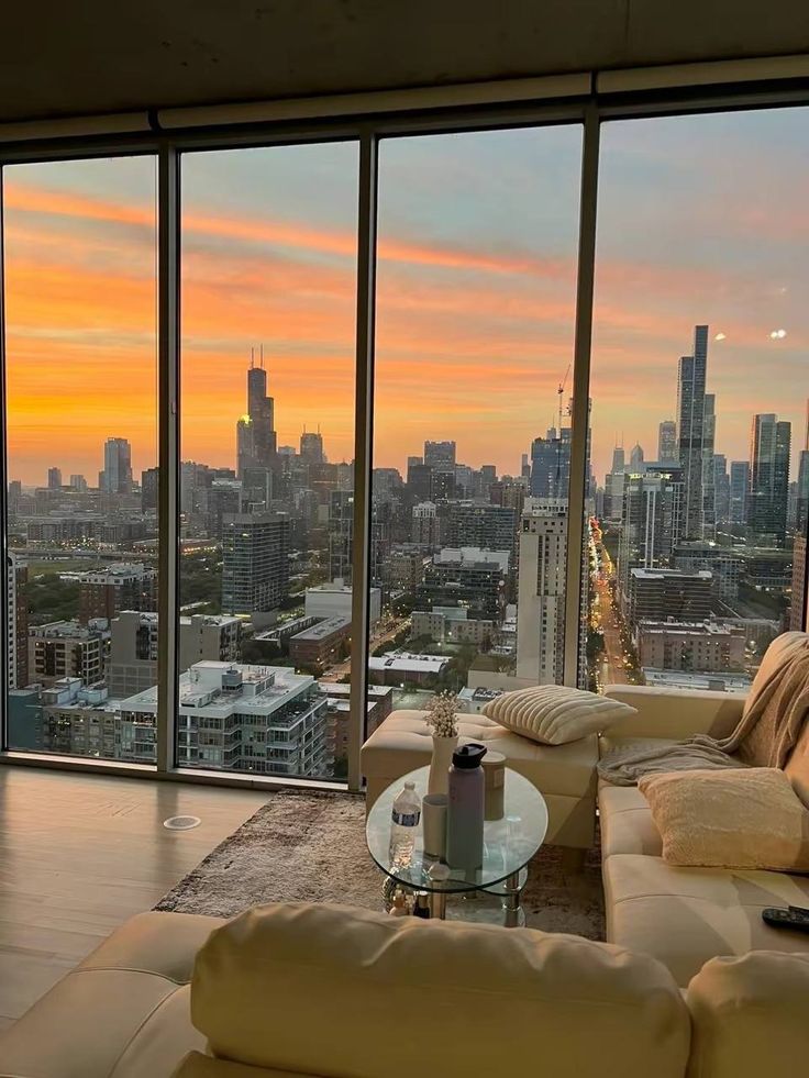 a living room filled with furniture and large windows overlooking a cityscape at sunset