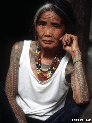 an old woman with tattoos on her arms and chest sitting in front of a door