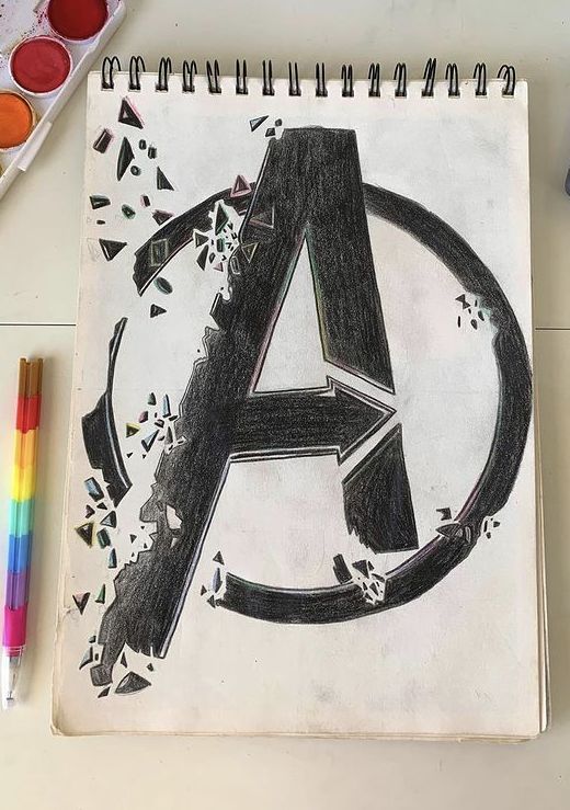 a drawing of the avengers logo with paint and crayons next to it on a table