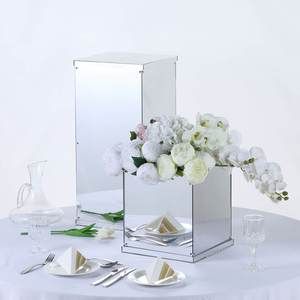 white flowers in a mirrored vase on a round table with plates and utensils