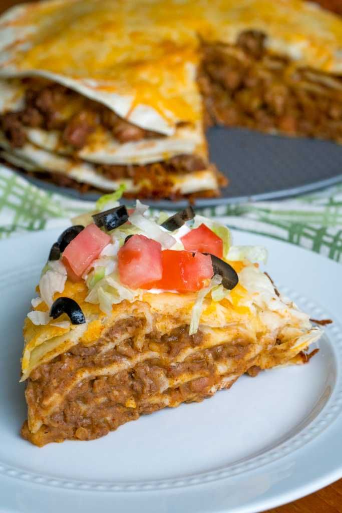 a slice of taco cake on a plate with the rest of the pie in the background