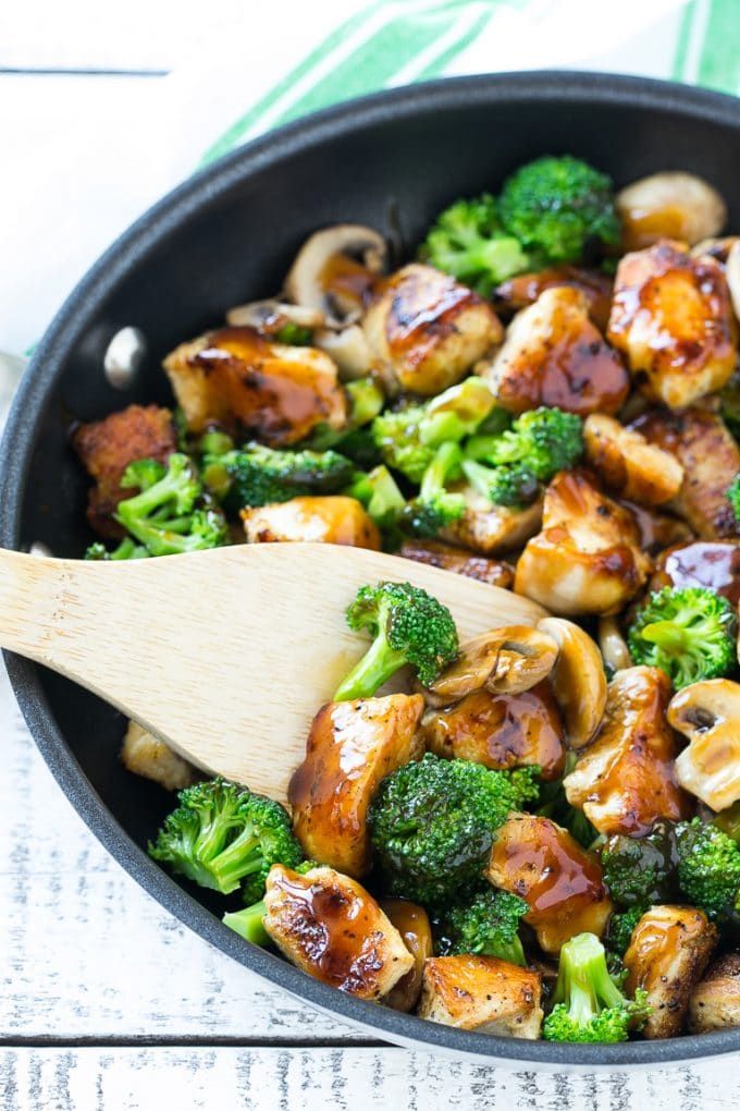 broccoli and chicken stir fry in a skillet with a wooden spatula