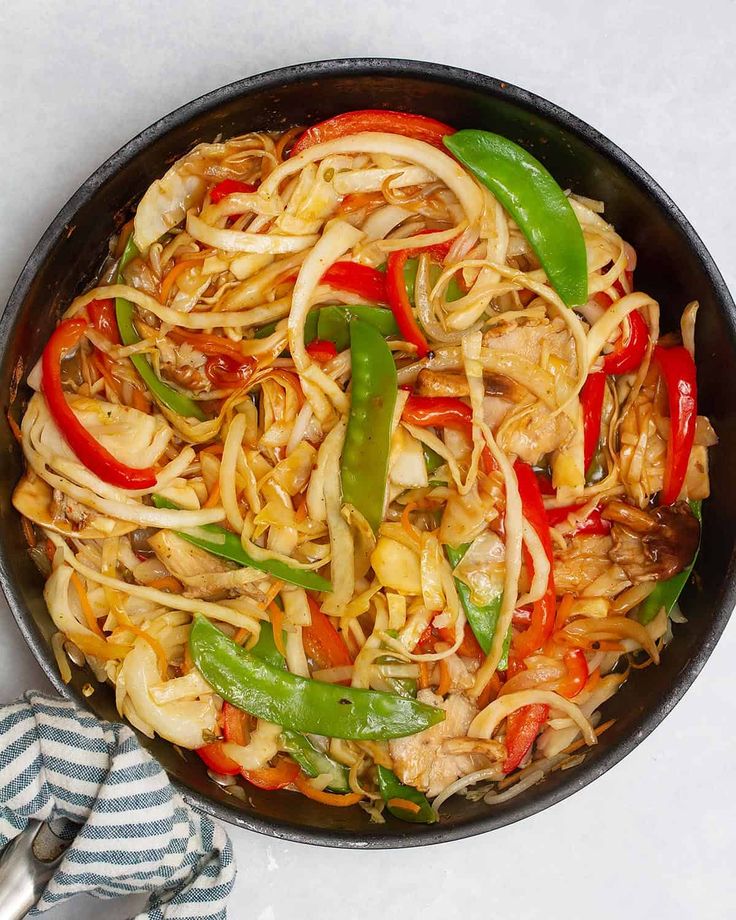 a pan filled with noodles and vegetables on top of a white countertop next to a striped towel