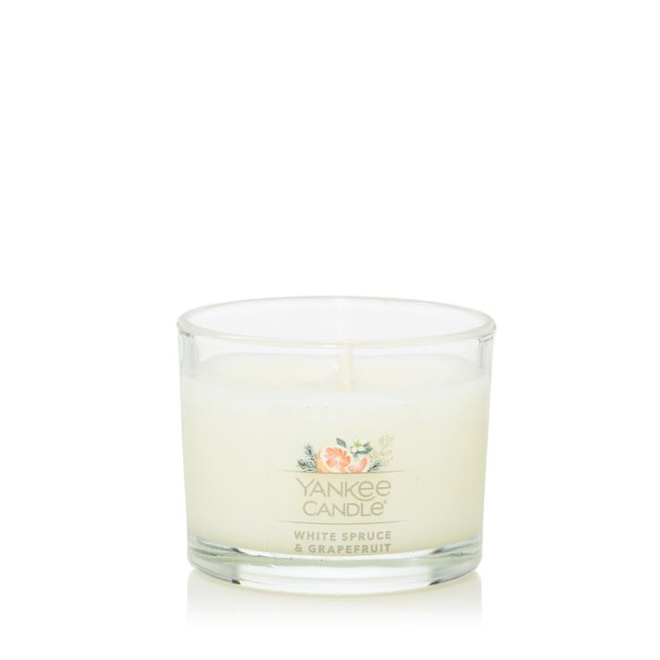 the yankee candle is white and has an orange flower on it's top, in front of a white background