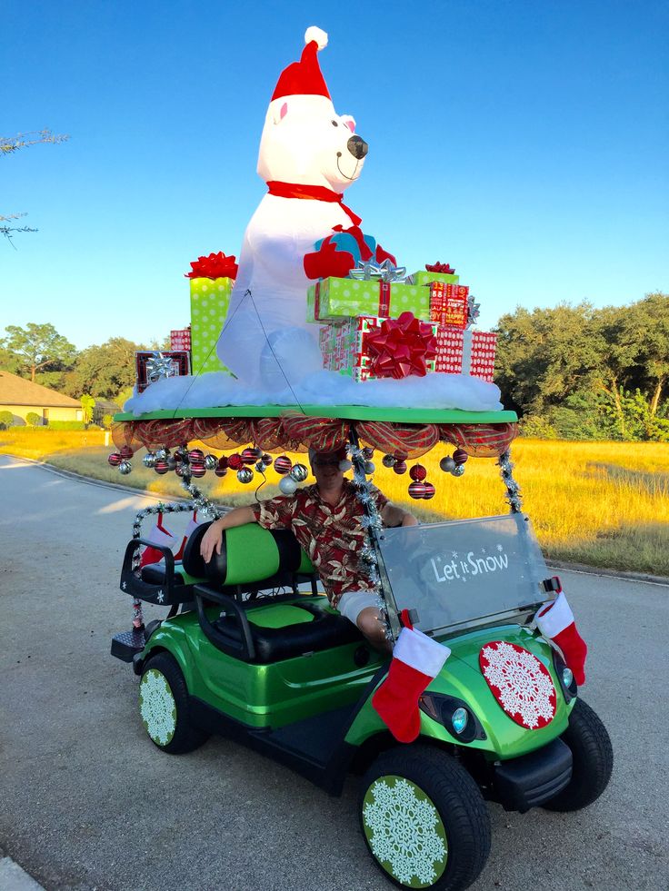 a person driving a golf cart with a large christmas bear on top