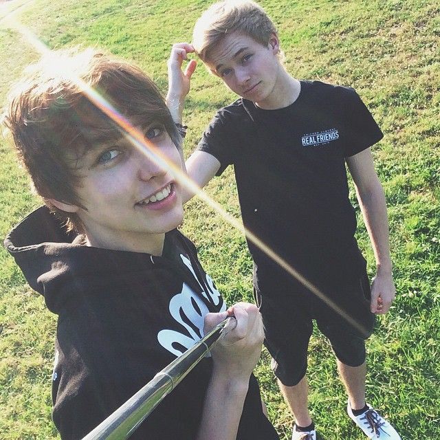 two young boys standing next to each other on top of a grass covered field holding baseball bats