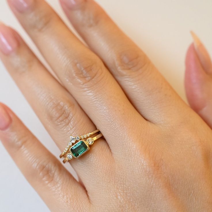 Jennie Kwon has managed to take a straightforward style—the classic solitaire with accent diamonds—and utterly transformed it with the inclusion of a brilliant green emerald at the center. The square band reflects the emerald cute stone, adding an unusual geometric edge to the ring. White diamonds flank the center stone on each side while a beaded bezel setting surrounds all the stones to add a gorgeous dose of texture. Emerald measures 6 mm x 4mm. 14 karat gold with an emerald and two white dia Jennie Kwon, Friendship Ring, Pink Diamond Ring, Emerald Ring Gold, Friendship Rings, Put A Ring On It, Green Emerald, Dainty Ring, Pink Diamond