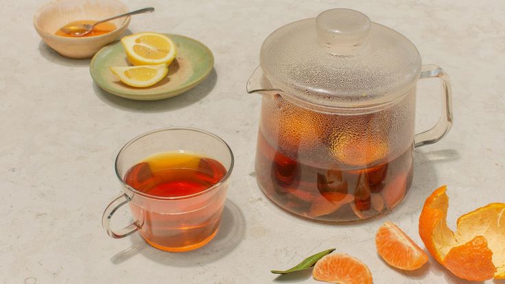 a tea pot filled with orange slices next to a cup of tea