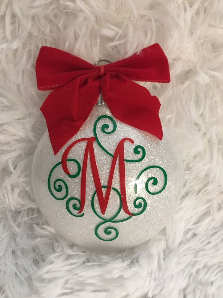 a white ornament with a red bow on it and the letter m painted on it