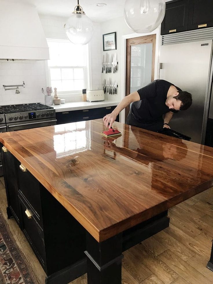 a man is sanding down on a wooden counter top in a kitchen with black cabinets and stainless steel appliances