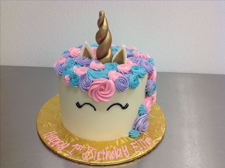 a birthday cake decorated with pink, blue and purple icing has a unicorn horn on top