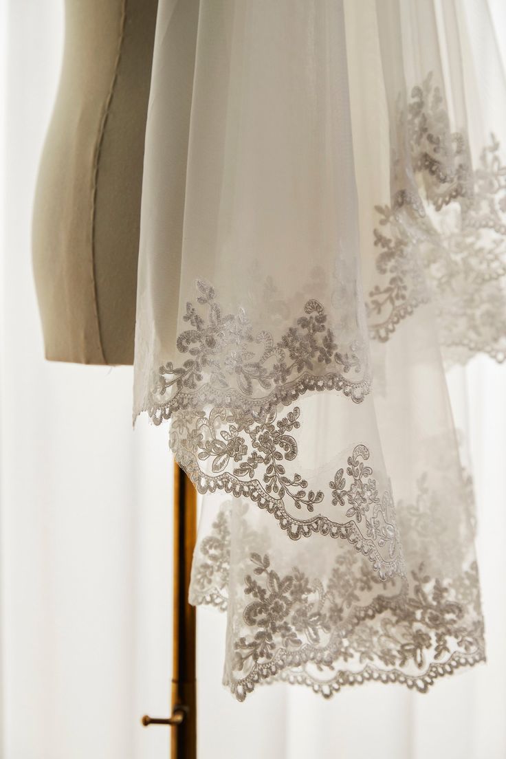 two white sheer curtains hanging from a wooden pole next to a dress mannequin