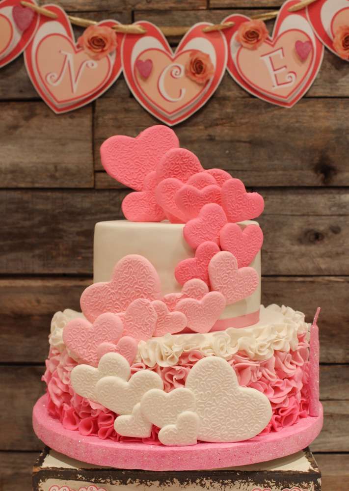 a pink and white cake with hearts on it sitting on top of a wooden table