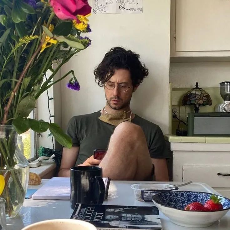 a man sitting at a kitchen counter looking at his cell phone with flowers in the background