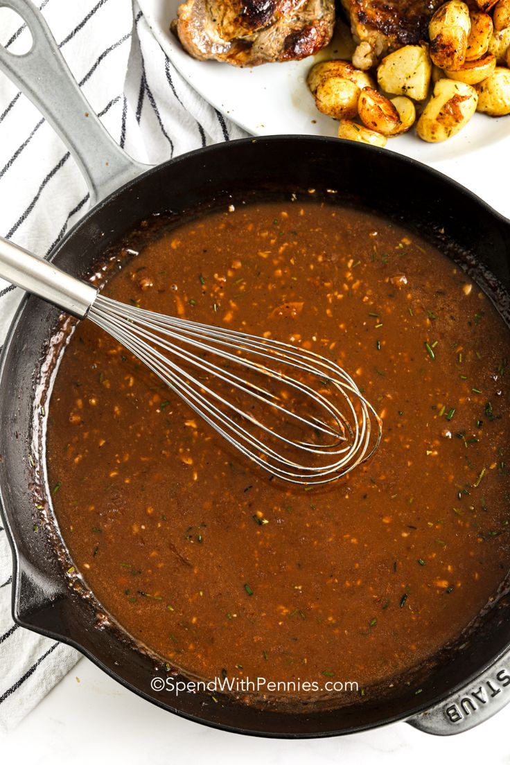 a skillet filled with sauce next to some meat and potatoes on a white table