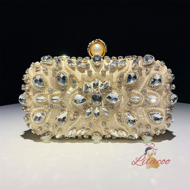 Illuminate your evening ensemble with this exquisite handbag, adorned with dazzling crystals and intricate beadwork. The bag features a stunning design with large teardrop crystals that catch the light beautifully, making it a perfect accessory for any special occasion. The central floral pattern, crafted with smaller crystals and beads, adds a touch of elegance and sophistication. The gold-tone metal frame and clasp, adorned with a pearl, provide a luxurious finishing touch. Inside, the bag is Sparkling Crystal Bags For Party, Crystal Clutch With Rhinestones For Party, Crystal Evening Bag With Bling For Party, Crystal Bling Evening Bag For Party, Crystal Evening Bag With Rhinestones For Parties, Glamorous Crystal Clutch For Party, Glamorous Crystal Clutch For Prom, Glamorous Crystal Evening Bag For Prom, Prom Evening Bag Embellished With Crystals