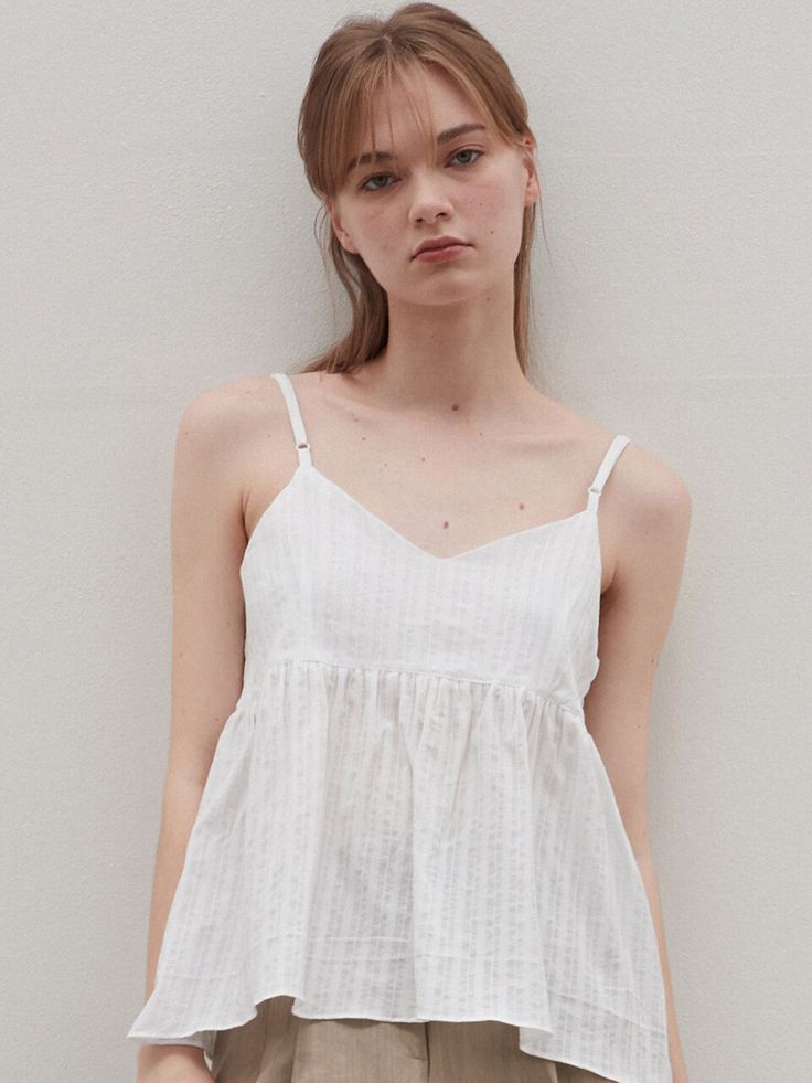 a woman standing in front of a white wall with her hand on her hip and looking at the camera