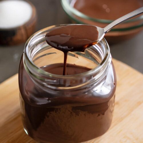 a spoon full of chocolate sauce sitting on top of a wooden cutting board