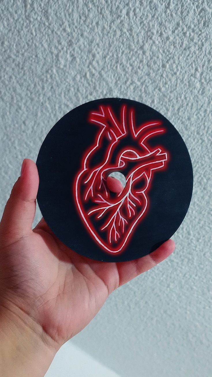 a hand holding a sticker with a neon heart on it's side, in front of a white wall