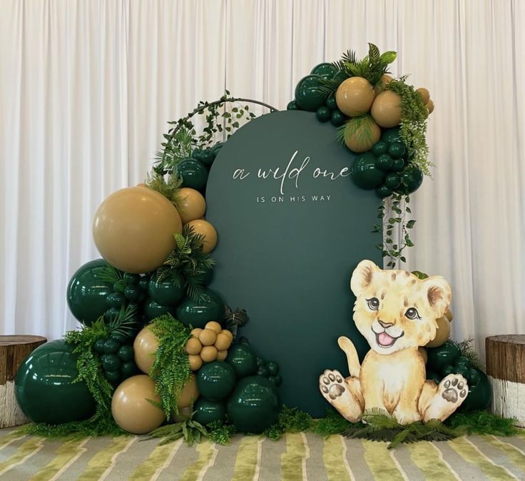 there is a fake lion sitting in front of a backdrop with balloons and greenery