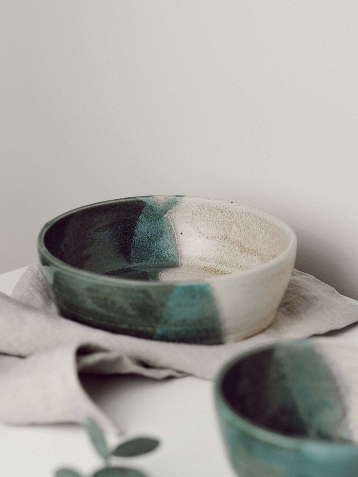 two green and white bowls sitting next to each other on top of a cloth covered table