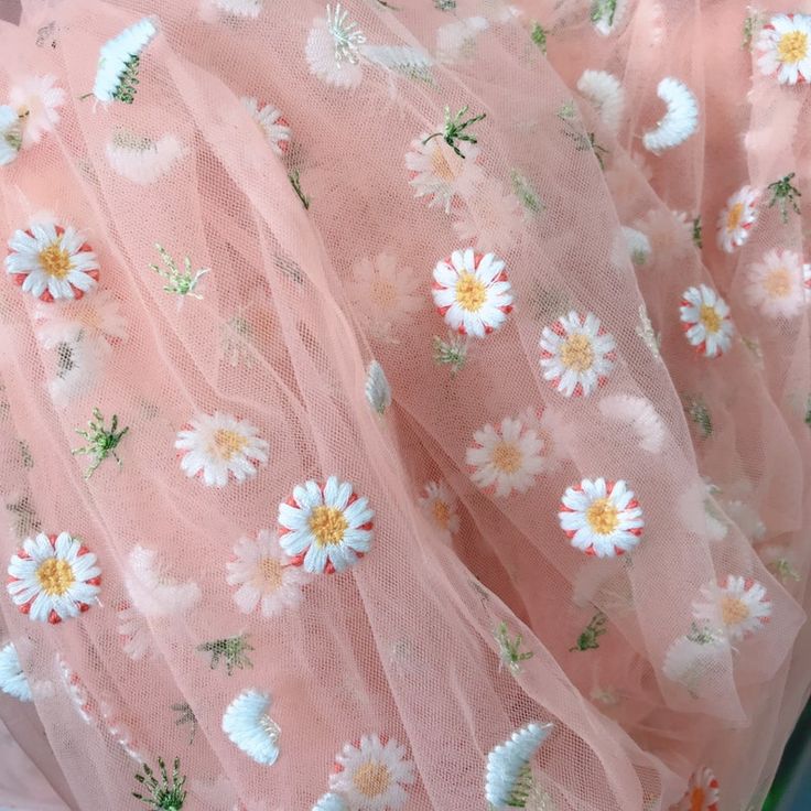 a pink dress with white daisies and green leaves on the bottom is shown in close up