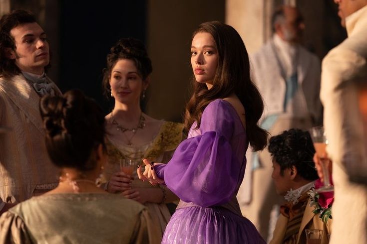 a woman in a purple dress standing next to other people and looking at each other