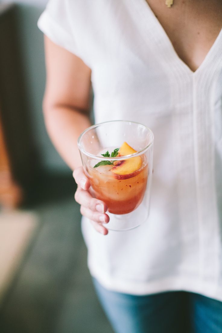 a woman holding a drink in her hand with fruit on the rim and garnish