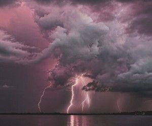 a lightning bolt is seen in the sky above water with dark clouds and purple hues