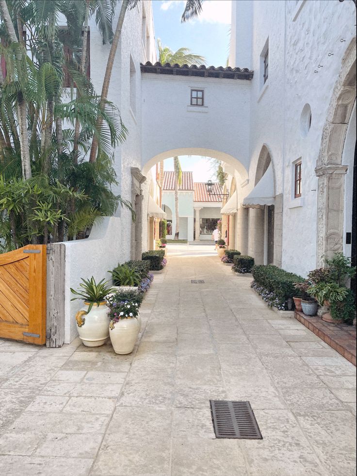 an archway leading into a white building with potted plants on either side and a wooden gate in the middle