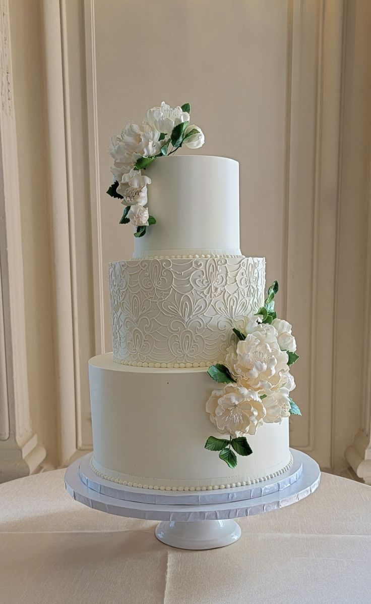 a three tiered wedding cake with white flowers on top is sitting on a table