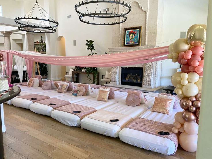 a large bed covered in lots of pillows and pink sheets with balloons hanging from the ceiling