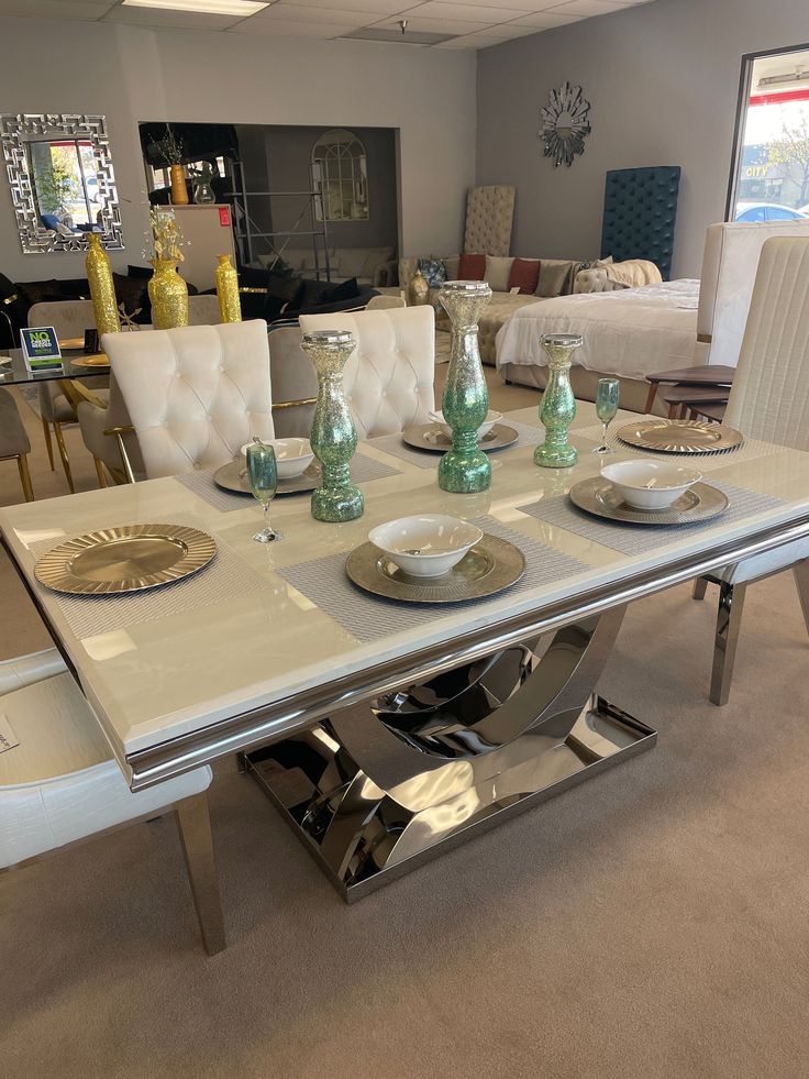 a glass table with white chairs and plates on it