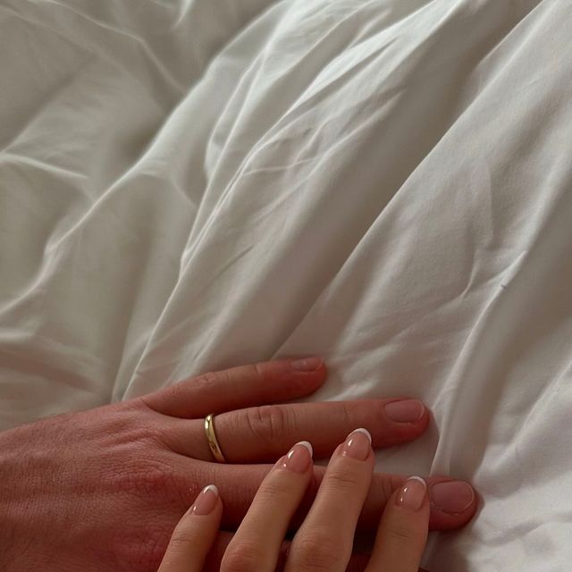 two hands touching each other on top of a white bed sheet covered in sheets and pillows