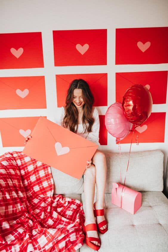 a woman sitting on top of a couch holding balloons and a heart cut out sign